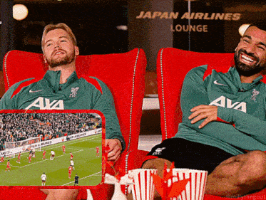 two men are sitting in red chairs with popcorn in front of a sign for japan airlines lounge