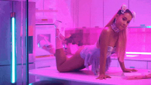ariana grande is kneeling on a table in a pink room in a video .