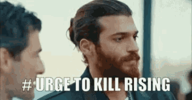 a man with a beard and a bun is standing next to another man and says `` urge to kill rising '' .