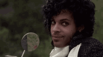 prince is smiling while sitting on a motorcycle with a lollipop in his hand .