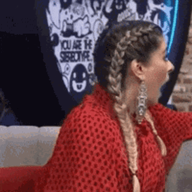 a woman in a red sweater with braids is sitting on a couch .