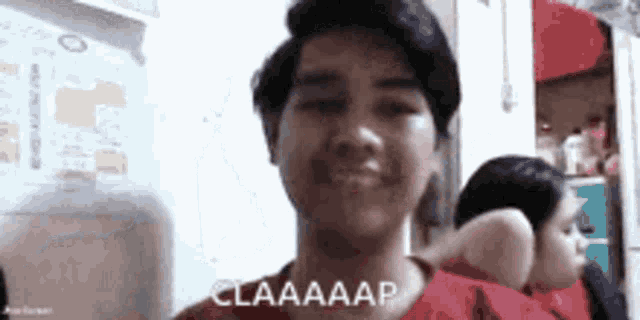 a young man in a red shirt is smiling and making a funny face while sitting in front of a mirror .