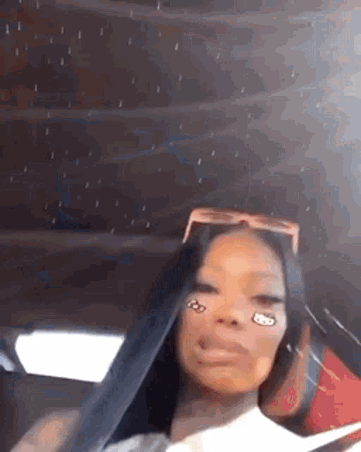 a woman is sitting in a car wearing sunglasses and making a face .