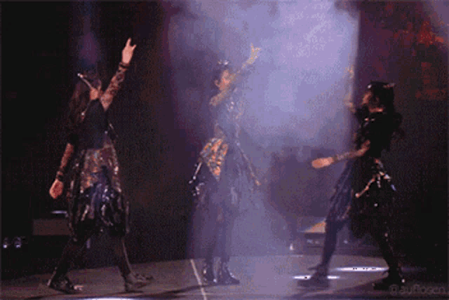 three women are dancing on a stage with smoke coming out of the bottom right