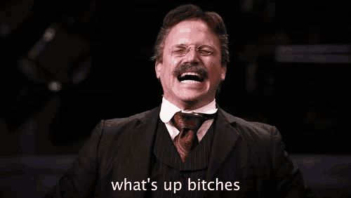 a man in a suit and tie is laughing with the words what 's up bitches written below him