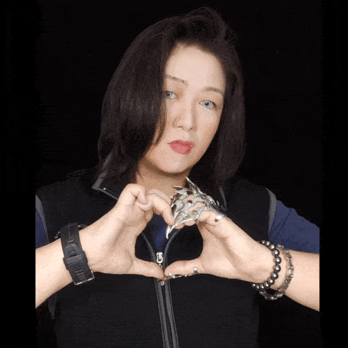 a woman wearing a black vest and bracelets holds a silver ring in her hands