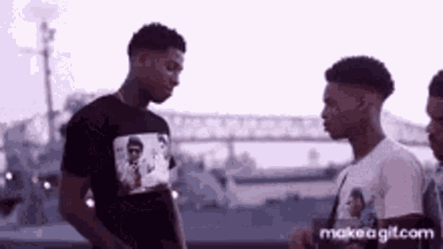 a group of young men are standing next to each other in front of a bridge and talking .