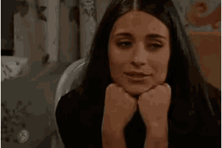 a woman is sitting in a chair with her hands on her chin and wearing a ring on her finger .