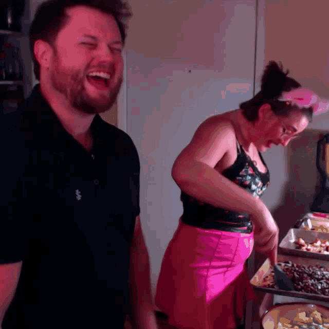 a man and a woman are laughing in a kitchen and the man is wearing a black shirt with the word eagle on it