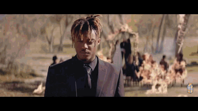 a man in a suit and tie is standing in front of a group of people in a cemetery .
