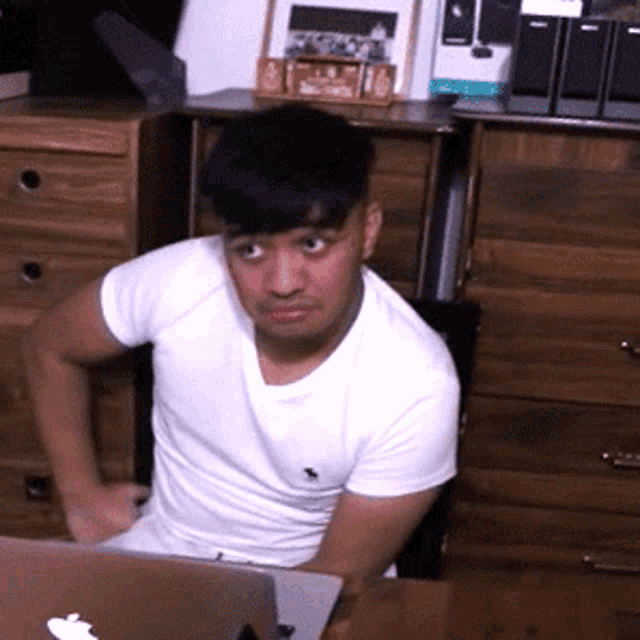 a man in a white shirt sits in front of a laptop