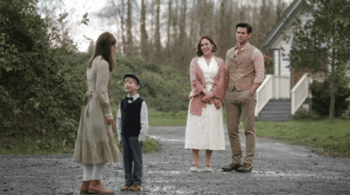 a family is standing on a dirt road in front of a white house