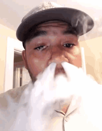 a man wearing a hat is blowing smoke from his mouth