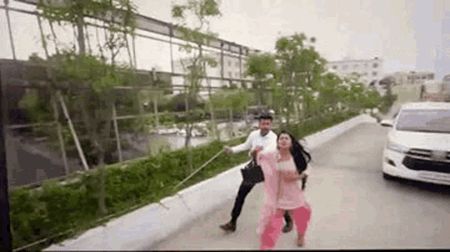 a man and a woman are walking down a street with a car behind them .