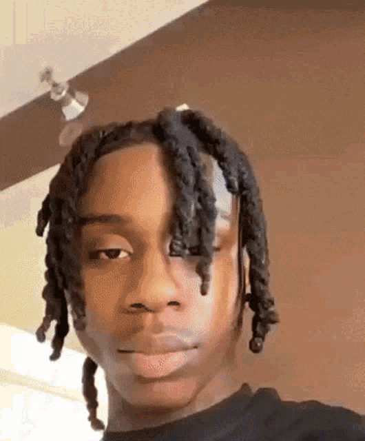 a young man with dreadlocks and a black shirt is looking at the camera .