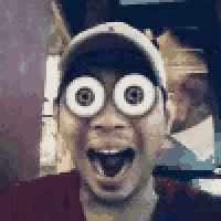 a man wearing a hat and glasses with big eyes is smiling .