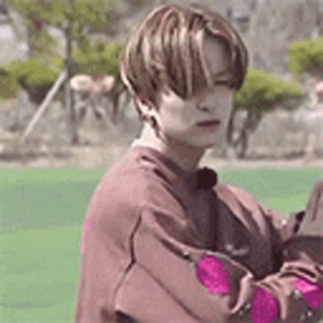 a young man wearing a brown sweater with pink sleeves is standing on a green field .