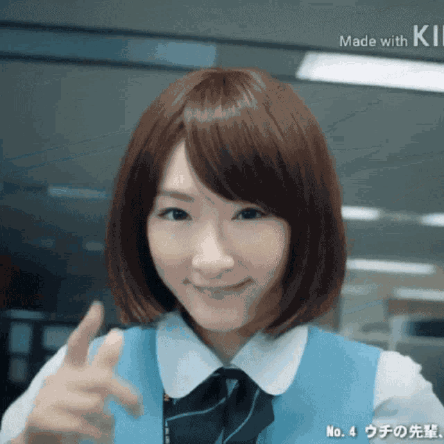 a woman wearing a blue vest and a white shirt is smiling and giving a peace sign