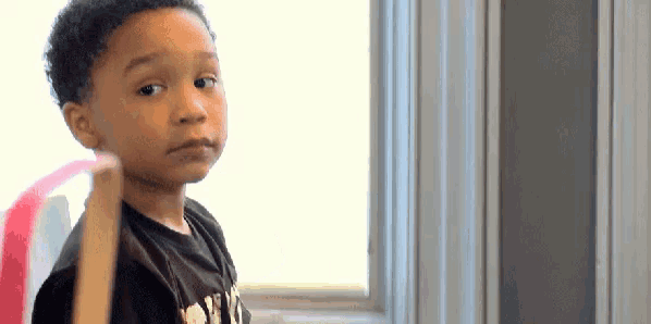 a young boy is standing in front of a window holding a pink object .