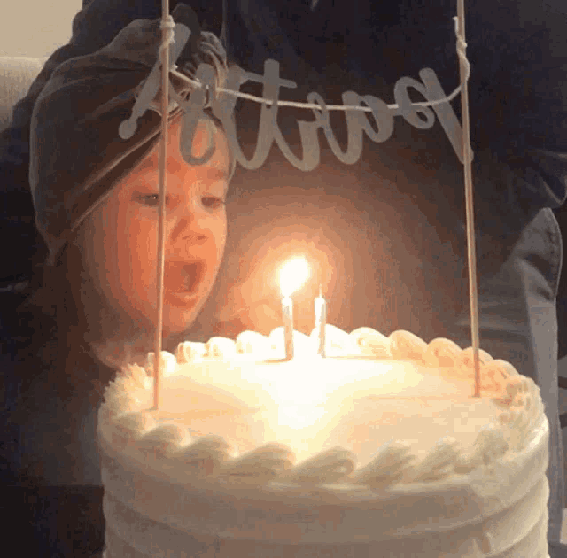 a little girl blows out a candle on a cake with the name ashton on it