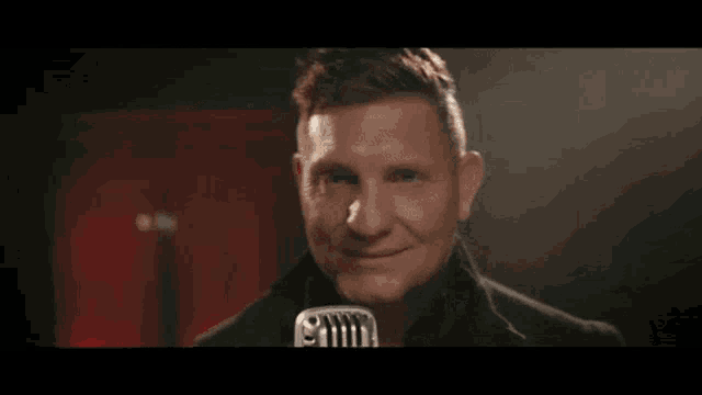 a man is smiling while holding a microphone in front of his face .