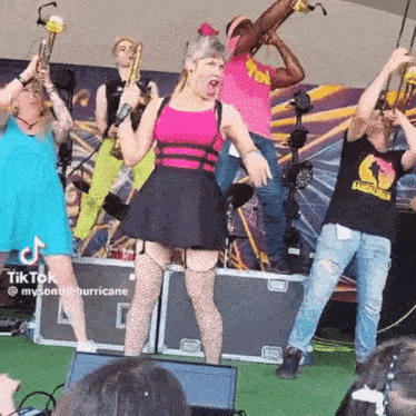 a group of people are standing on a stage playing instruments and dancing .