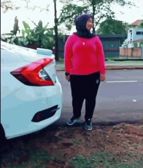 a woman in a pink sweater is standing next to a white car .
