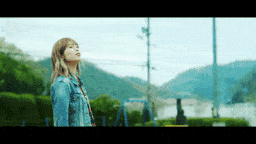 a woman in a denim jacket is standing in front of a playground with mountains in the background