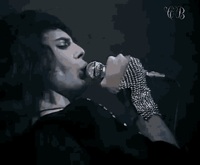 a man is singing into a microphone while wearing a chain bracelet on his wrist .