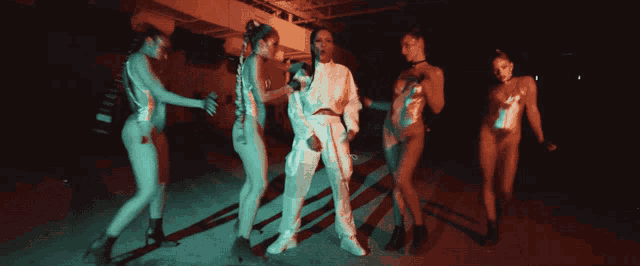 a man in a white suit is surrounded by a group of naked women