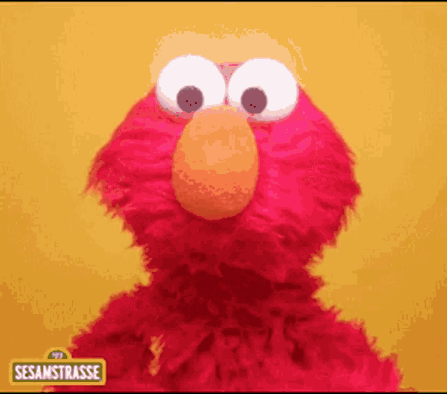 elmo from sesame street is standing in front of a yellow wall .