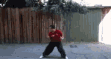 a man in a red shirt and black pants is dancing in a parking lot .
