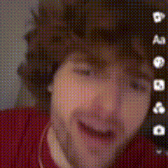 a man with curly hair and a beard is wearing a red shirt and a necklace .