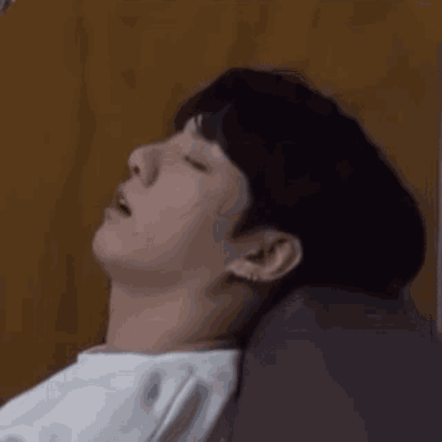 a young man is laying on a bed with his eyes closed and his mouth open .