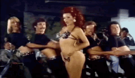 a woman in a bikini is dancing in front of a group of men in black shirts .