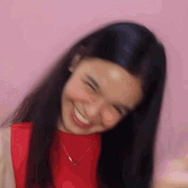 a woman with long black hair is wearing a red shirt and a necklace and smiling .