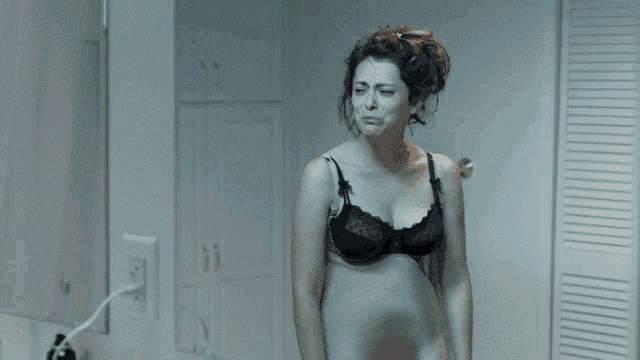 a woman in a black bra is crying in front of a bathroom mirror