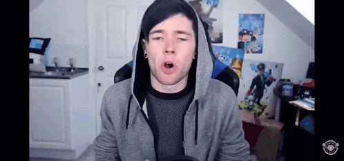 a man wearing a grey hoodie is sitting in front of a wall with posters on it