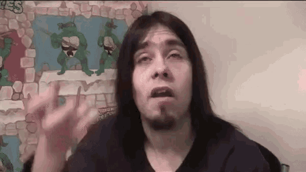 a man with long hair and a beard is making a face in front of a teenage mutant ninja turtles poster .