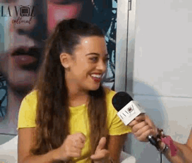 a woman in a yellow shirt is talking into a microphone while smiling .