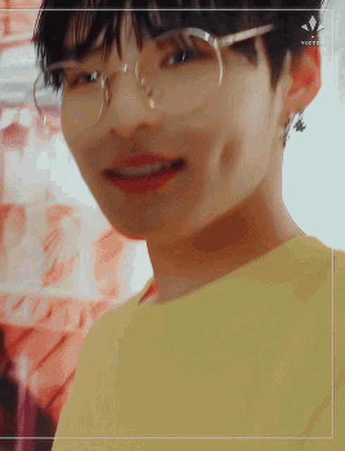 a young man wearing glasses and a yellow shirt smiles for the camera