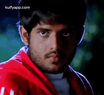 a young man with a beard wearing a red jacket is looking at the camera .