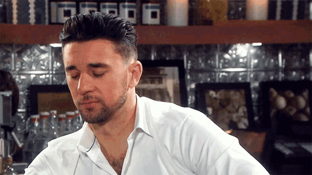 a man with a beard wearing a white shirt is sitting at a counter