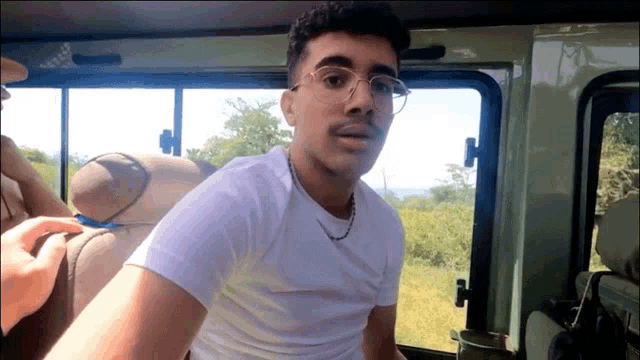 a man wearing glasses and a white shirt is sitting in the back seat of a vehicle