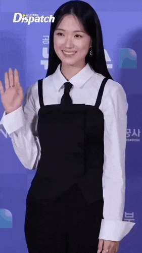 a woman in a black dress and tie is smiling and waving .