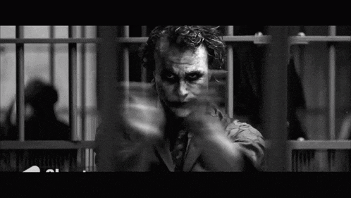 a black and white photo of the joker in a jail cell pointing at the camera .