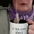 a woman is holding a cup of coffee with a spoon in it and a purple scarf around her neck .