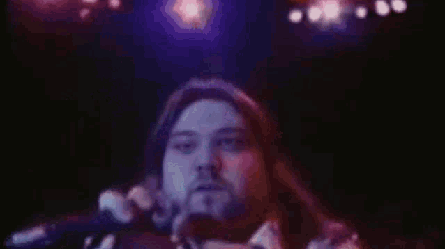 a man with long hair and a beard is sitting on a stage in front of a crowd .