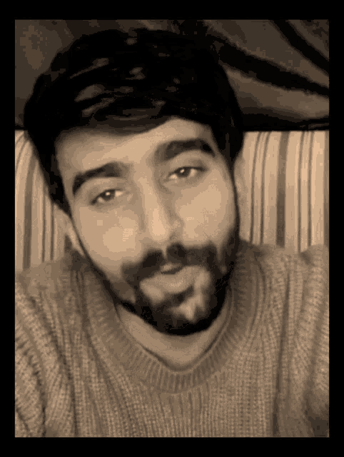 a man with a beard is wearing a sweater and looking at the camera