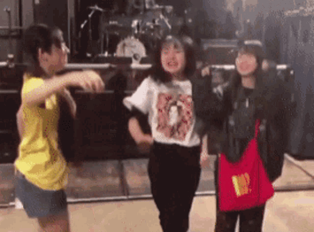 three girls are dancing in front of a drum set and one has a mcdonalds bag